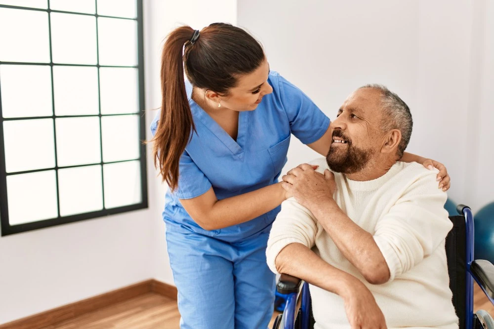 Disabled man in wheelchair looking up at nurse with hands clasped