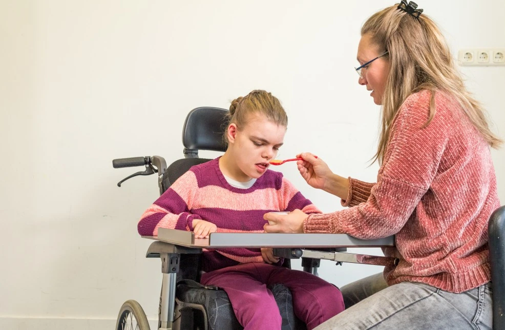 Disabled girl in wheelchair being fed by support worker