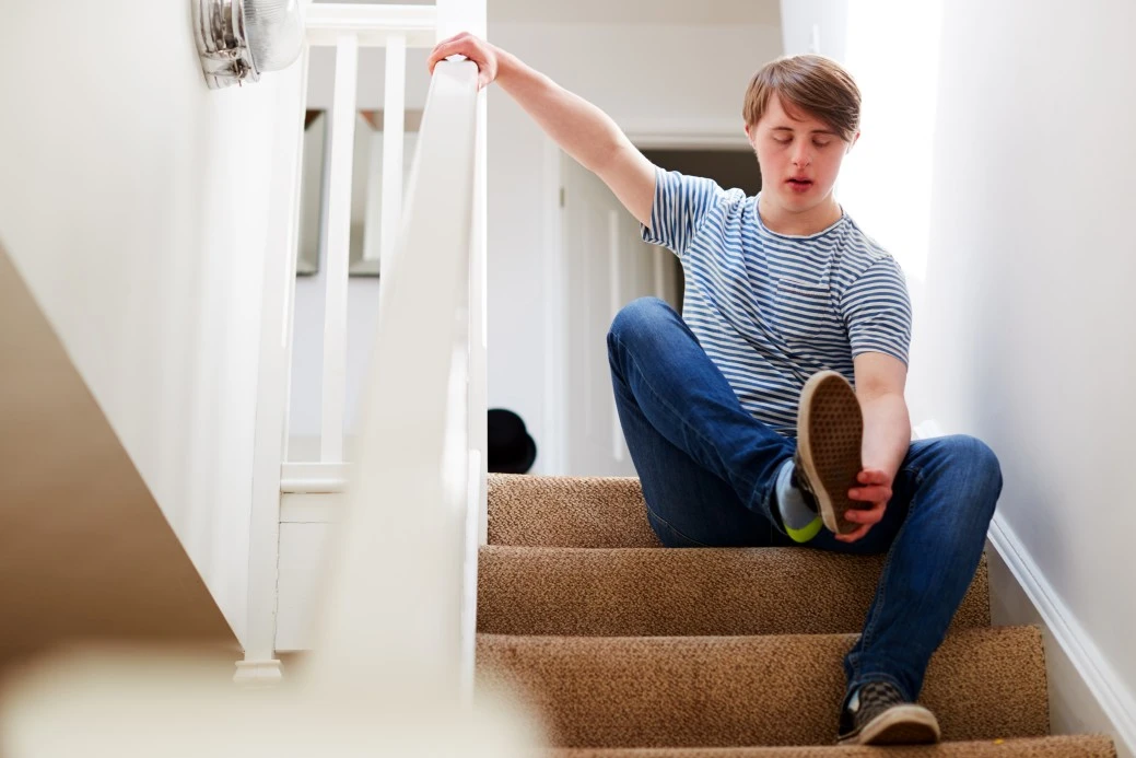 Disabled man with down syndrome sitting on stairs putting shoe on
