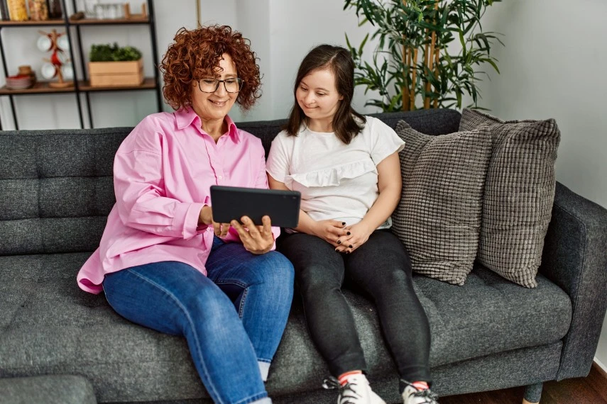 Disabled woman with down syndrome sitting on couch with support worker both looking at iPad
