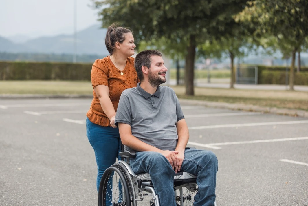 Disabled man in wheelchair outside in carpark with support worker, both smiling
