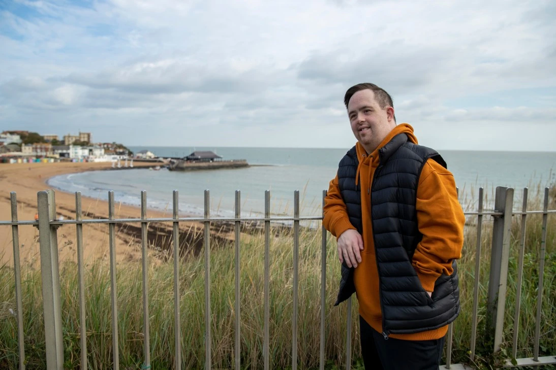 Disabled man with down syndrome leaning on fence at beach