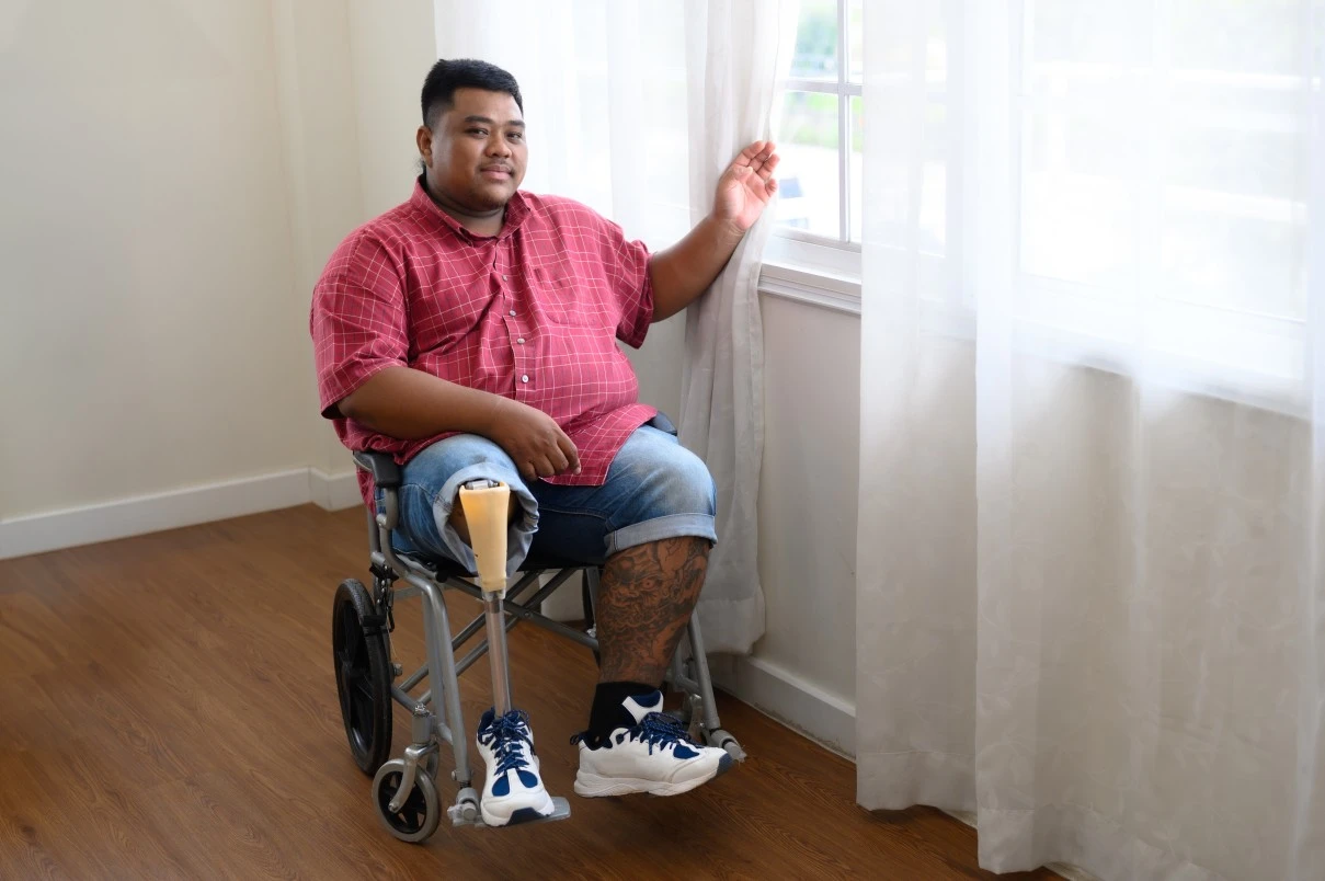 Disabled man in wheelchair sitting in room next to window and smiling at camera